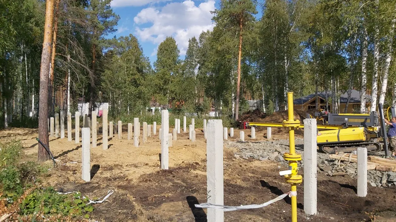 Свайное поле до подрезки оголовков: железобетонные сваи забиты на разную глубину и стоят на разной высоте, справа сваебойная установка